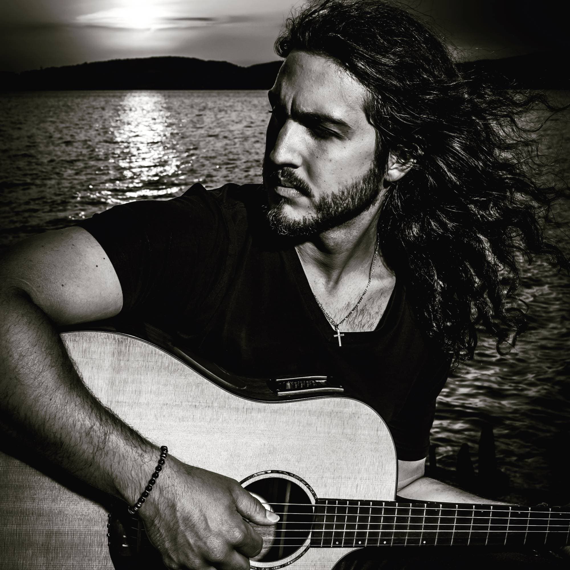 Alex Cano playing acoustic guitar by the water